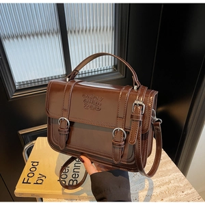 Close-up of a brown leather crossbody bag with vintage metal buckles and embossed texture