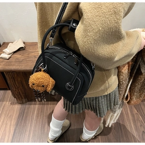 Detail of black leather bowling bag with white contrast stitching and a plush dog charm
