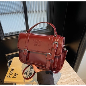 Detail of dark red vintage handbag showing glossy texture and silver buckle accents