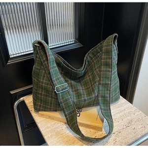 Detail of adjustable wide shoulder strap with silver buckle on green plaid tote bag