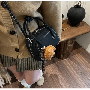 Detail of black leather bowling bag with white stitching and cute brown dog plush charm