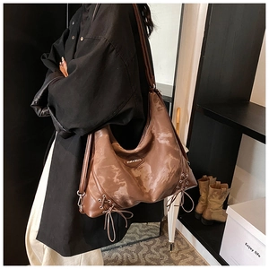 Detail of a large brown glossy tote bag featuring vintage texture and lace-up drawstring sides