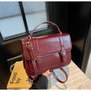 Macro view of burgundy matte leather flap bag with vintage buckles and embossed text