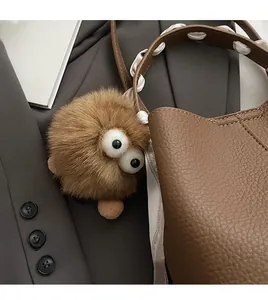 Brown fuzzy monster bag charm with large eyes attached to a leather bucket bag handle
