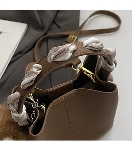 Close-up of brown bucket bag with silk scarf handle and plush ball charm accessory
