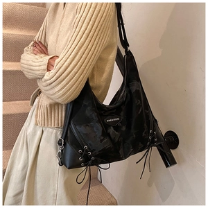 Detail view of large black tote bag featuring glossy patent texture and bow strap design