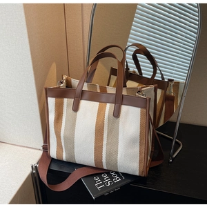 Detail of striped canvas tote bag showing the leather handles and woven texture finish