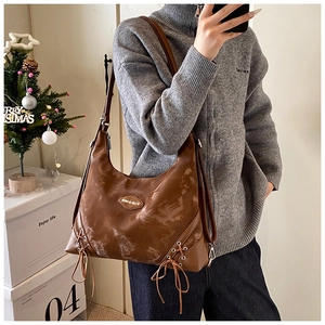Detailed close-up of brown oversized hobo bag featuring decorative side drawstrings and logo plaque