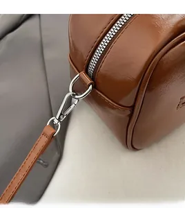 Close-up of brown leather bag showing detachable metal rings and sturdy zipper detail