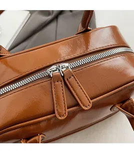 Detailed close-up of the smooth dual silver zippers on a brown glossy leather handbag