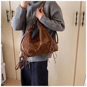 Detail of a brown leather crescent shoulder bag with silver eyelets and drawstring accents