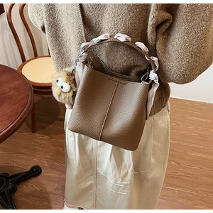 Detail of a brown lychee pattern bucket bag with a floral scarf and plush monster charm