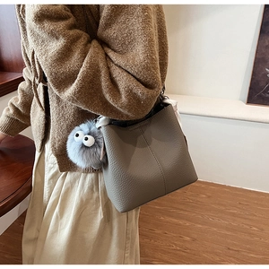 Detail of grey bucket bag with vertical stitching, plush charm and decorative silk scarf