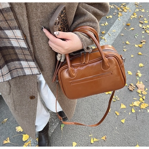 Close-up of vintage brown glossy Boston bag on ginkgo leaves background with shoulder strap