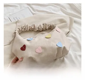 Detail of beige pleated shoulder bag with colorful heart patches in a cozy home setting
