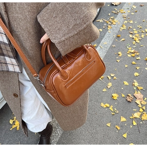 Close-up of brown patent leather handbag with thin shoulder strap on autumn leaves