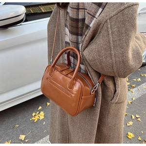 Caramel brown Boston handbag with double handles shown in a stylish autumn street scene