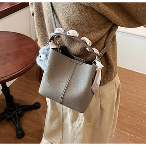 Detail view of taupe bucket bag with geometric silk scarf and plush pompom charm