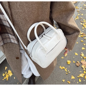 Chic glossy white patent leather boston bag on brown coat with autumn leaves background