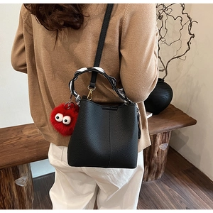 Detail of black leather bucket bag with silk scarf handle and red plush monster charm