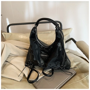 Detail of black leather half-moon tote with brand logo and side drawstring on a sofa