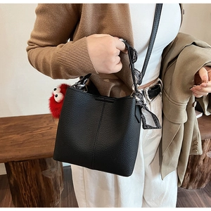 Detail of black lychee grain leather bucket bag featuring a silk scarf and red plush charm