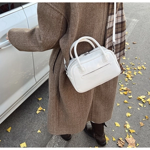 Close-up of white leather satchel with dual handles on autumn ground with ginkgo leaves