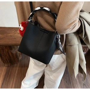 Detail of black pebbled leather bucket bag with patterned scarf and red plush charm