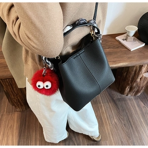 Detail of black pebbled leather bucket bag with decorative scarf and red plush charm