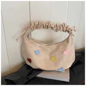 Detail of cream crescent bag featuring colorful heart patches and ruffled handle strap