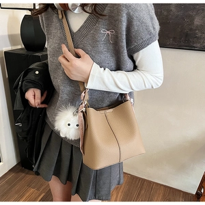 Detail of camel bucket bag in lychee pattern leather with cute white plush ball pendant