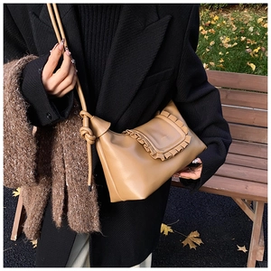 Detail of light brown crossbody bag featuring ruffled flap edges and knotted strap design