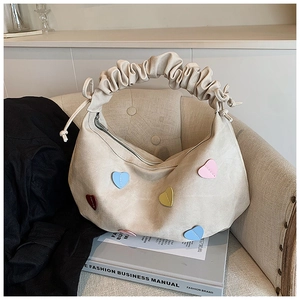 Detail of beige shoulder bag featuring colorful heart patches and pleated cloud handle
