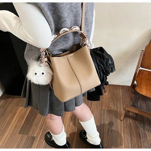 Girl carrying a camel bucket bag with printed scarf handle and white plush charm detail