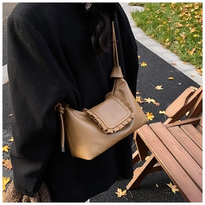 Detail of camel brown crossbody bag featuring pleated edges and adjustable strap on model