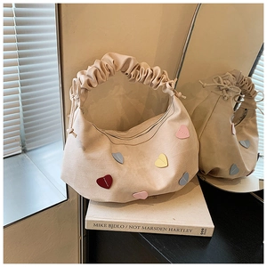 Detail of beige crescent canvas bag featuring colorful heart patches and pleated cloud handle