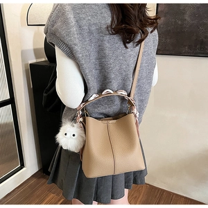 Khaki bucket bag with silk scarf handle and pompom charm worn by a model from a side view