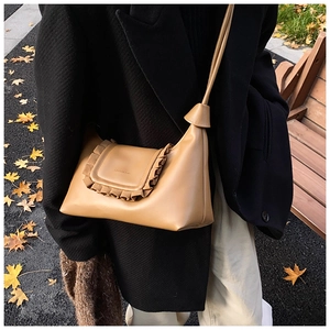 Detail of khaki leather shoulder bag featuring ruffle trim and matte finish on autumn backdrop