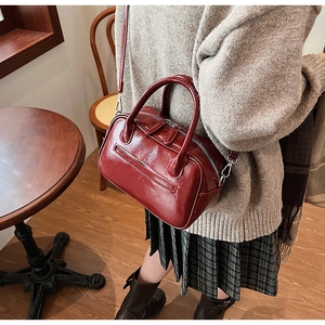 Detail of burgundy faux leather crossbody bag with dual zippers and silver hardware