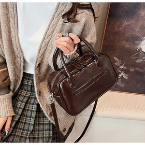 Detail of premium brown glossy leather handbag with dual zippers and round handles