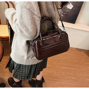 Chocolate brown patent leather crossbody bag shown on a model in a warm home setting