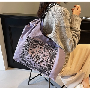 Detail of purple paisley drawstring tote bag with black and white woven shoulder strap