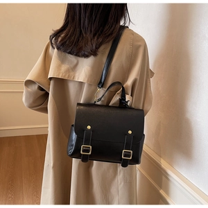 Classic British style black leather backpack with gold buckles worn by a model in a room