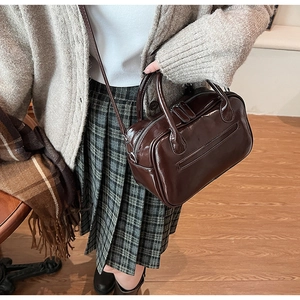 Detailed view of glossy dark brown faux leather bag with top handles and shoulder strap