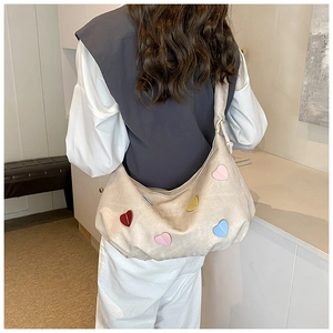 Detail of a beige crescent bag featuring colorful heart patches and wide shoulder strap