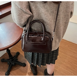 Detail view of dark brown patent leather handbag showing sleek crossbody styling on model