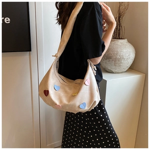 Close-up of beige shoulder bag featuring colorful heart patches and thick strap detail