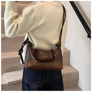 Detail view of brown faux leather shoulder bag featuring pleated edges and knotted strap