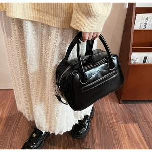 Detail of a black glossy leather handheld Boston bag with silver zipper and lifestyle styling