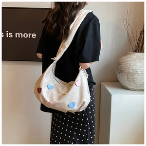 Detail of off-white canvas shoulder bag featuring colorful heart patches and wide strap